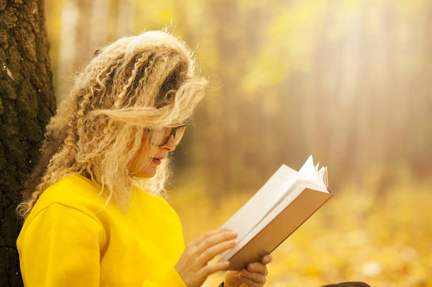 美しい女子学生は、暖かい太陽の光線で秋の公園で一人で本を読みます。レッスンを行う教育の概念 - 写真・画像