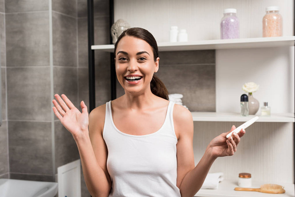 excited brunette woman holding pregnancy test in bathroom  - Foto, imagen