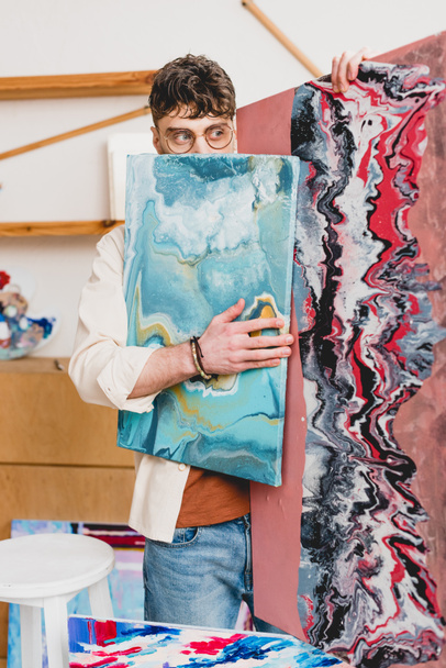 selective focus of artist in eyeglasses hiding face behind colorful painting  - Photo, Image