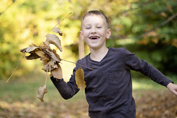 mosolygós ifjú fiú elülső fogak nélkül játszik a levelek - Fotó, kép