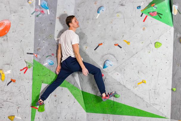 Rock climber man hanging on a bouldering climbing wall, inside on colored hooks - Photo, Image