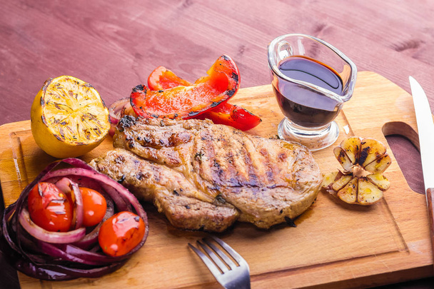 steak de porc juteux avec un brin de thym frais, citron et légumes grillés et sauce servie sur une planche en bois
 - Photo, image