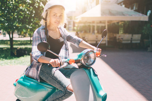 Young cheerful girl driving scooter in in city. Portrait of a young and stylish woman with a moped - Zdjęcie, obraz