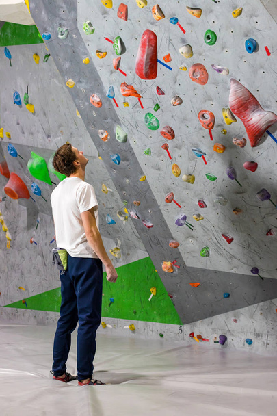 Rock climber stands and looks at the climbing wall with hooks in the boulder hall - Foto, Imagem