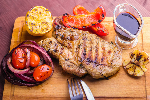 Carne de cerdo jugosa con una ramita de tomillo fresco, limón y verduras a la parrilla y salsa servida en una tabla de madera
 - Foto, imagen