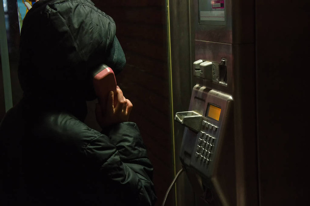 muž v černé bundě dělá noční hovor z telefonní budky - Fotografie, Obrázek