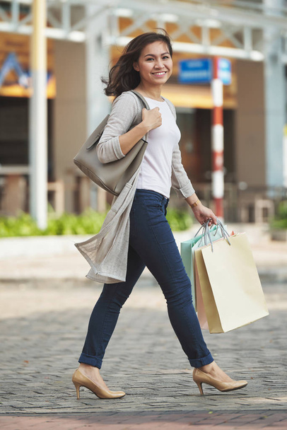 Досить щаслива молода жінка з паперовими мішками, що ходять на вулиці після шопінгу весь день
 - Фото, зображення