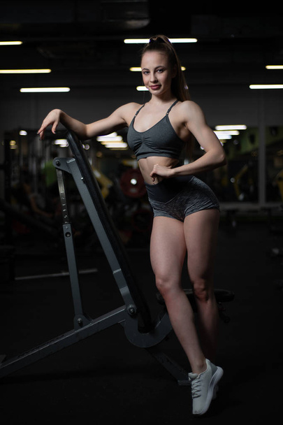 Фітнес дівчина позує в спортзалі на лавці, показуючи її тіло
 - Фото, зображення