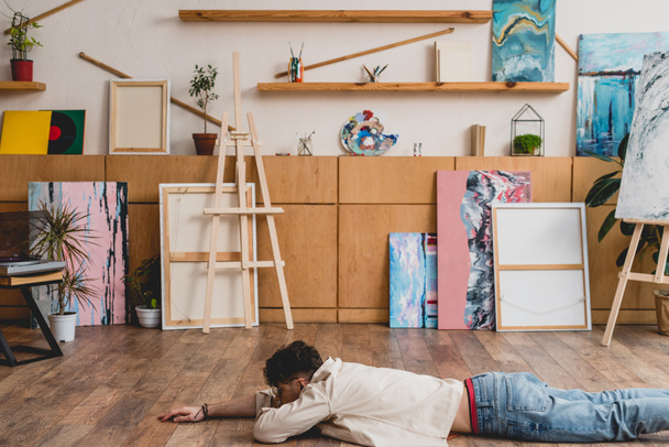 artiste couché face contre terre sur le sol en bois dans un studio de peinture spacieux
 - Photo, image