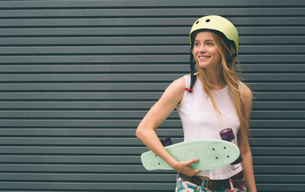 Young blonde woman with a skateboard in his hand against the background of a Striped wall - Photo, Image