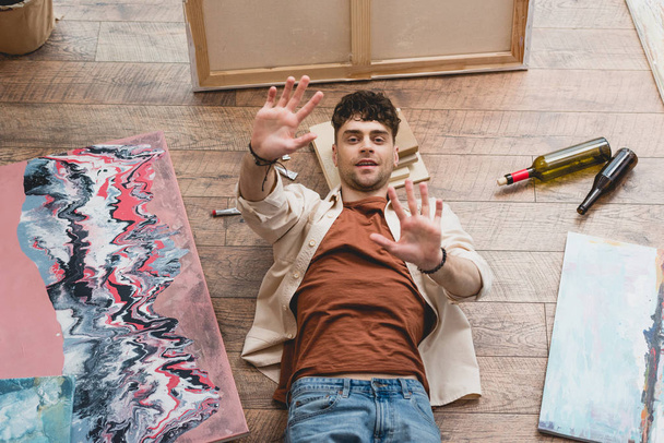 overhead view artist lying on wooden floor with stretched hands - Photo, Image