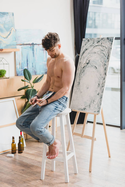 half-naked handsome artist sitting on chair in painting studio - Photo, Image
