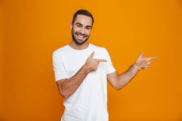 Image of smiling guy 30s in t-shirt pointing fingers aside while - Valokuva, kuva