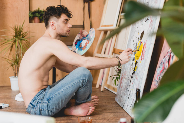 selective focus of thoughtful half-naked artist holding palette and painting picture - Foto, afbeelding
