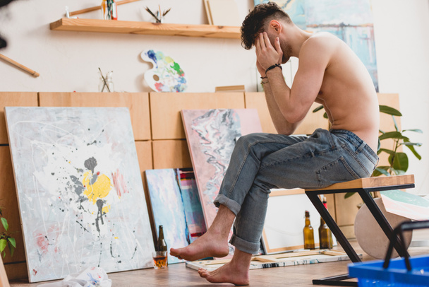 kimerült művész ül a széken a festészet stúdió, és tartja a kezében a fej - Fotó, kép