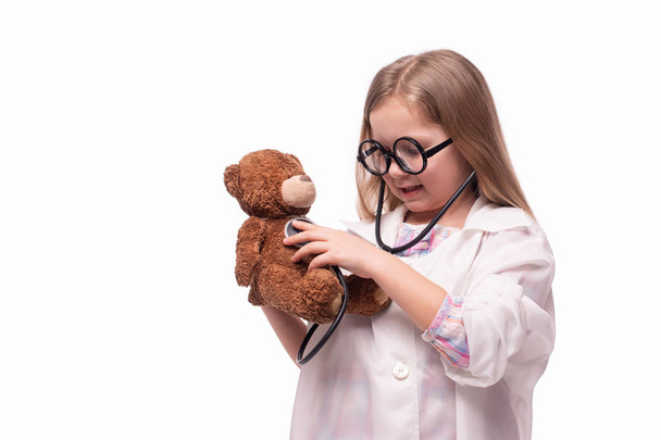 Студийный снимок маленькой улыбающейся девочки в белом медицинском халате
 - Фото, изображение