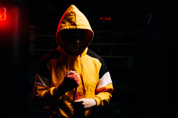 Woman boxer in hood pulls red bandages on hands. - Fotó, kép