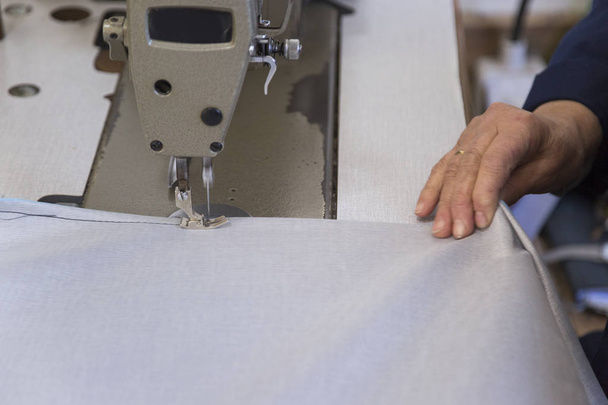 Κοντινό πλάνο του μια ηλικιωμένη γυναίκα σε ένα εργοστάσιο επίπλων που ράβει το υλικό για τον καναπέ - Φωτογραφία, εικόνα