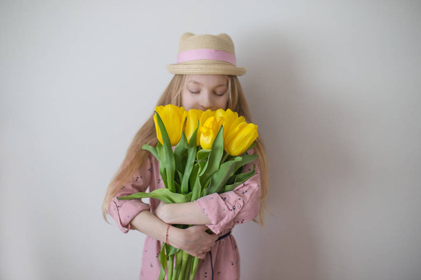 黄色のチューリップをかぐ十代の少女、花に焦点を当てる - 写真・画像
