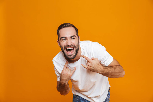 Image of happy guy 30s in t-shirt rejoicing and showing rock sig - Foto, immagini
