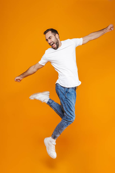 Full length photo of attractive guy in t-shirt and jeans jumping - Фото, изображение