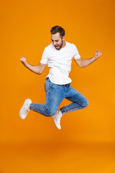Full length photo of smiling guy in t-shirt and jeans jumping an - Фото, изображение