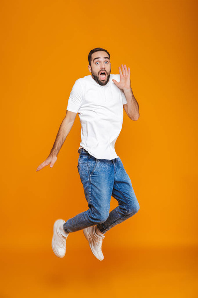 Full length photo of scared guy in t-shirt and jeans jumping and - Foto, Imagem