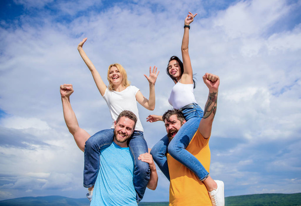 We are the winners. Happy men piggybacking their girlfriends. Loving couples enjoy fun together. Playful couples in love smiling on cloudy sky. Loving couples having fun activities outdoor - Photo, Image