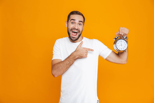 Photo of brunette man 30s in casual wear holding alarm clock, is - Fotoğraf, Görsel