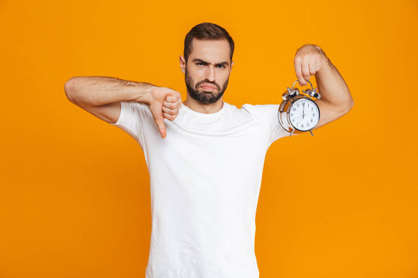 Photo of upset man 30s in casual wear holding alarm clock, isola - Фото, изображение