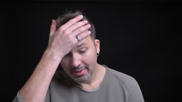Portrait of middle-aged caucasian man with earring gesturing facepalm sign to show annoyance into camera on black background. - Footage, Video