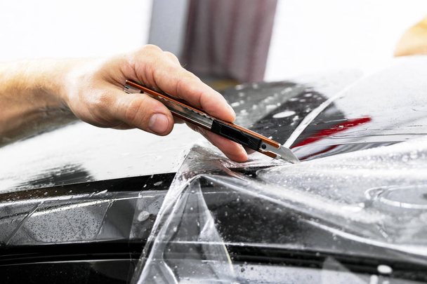Car wrapping specialist cutting vinyl foil or film on car. Protective film. Applying a protective film with tools for work. Car detailing. Transparent film. Car paint protection. Trimming.  - Photo, image