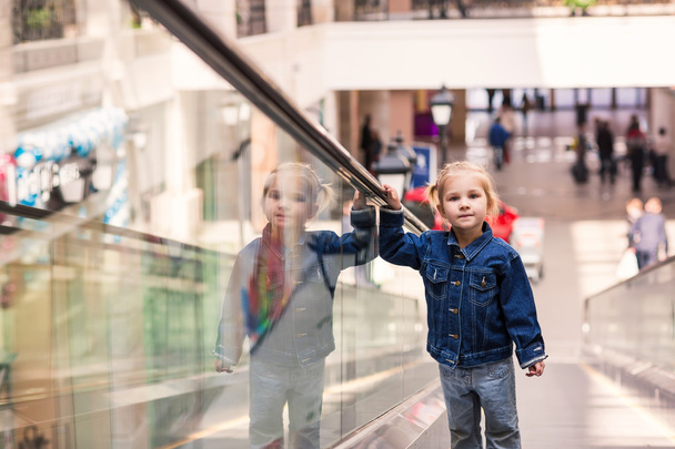 Lindo niño pequeño en el centro comercial de pie en la escalera mecánica en movimiento
 - Foto, imagen