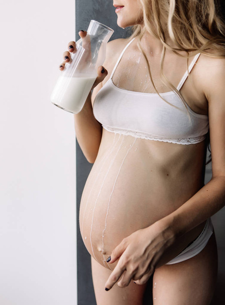 menina loira grávida em roupa interior branca bebe leite de uma garrafa e derrama em si mesma
 - Foto, Imagem