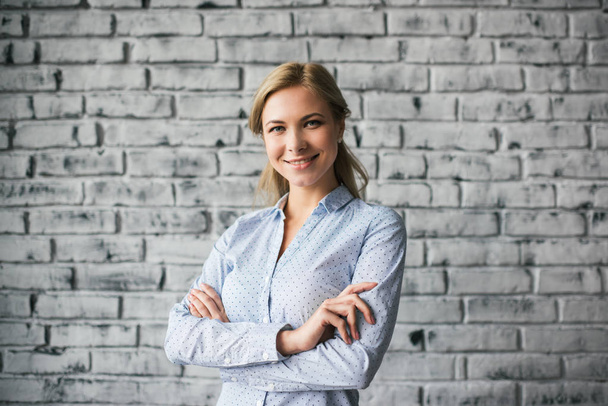 Happy businesswoman with arms crossed  posing for pictures in loft office isolated on background. Successful business concept. Portrait of young cheerful top manager or team leader - Photo, Image