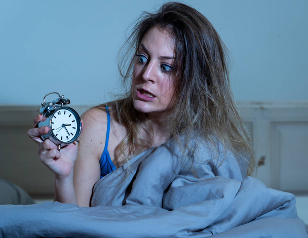 Slapeloze en wanhopig mooie Kaukasische vrouw wakker in de nacht niet kunnen slapen, weergegeven: de klok, gevoel gefrustreerd en ongerust lijden aan slapeloosheid in slaap stoornis concept. - Foto, afbeelding