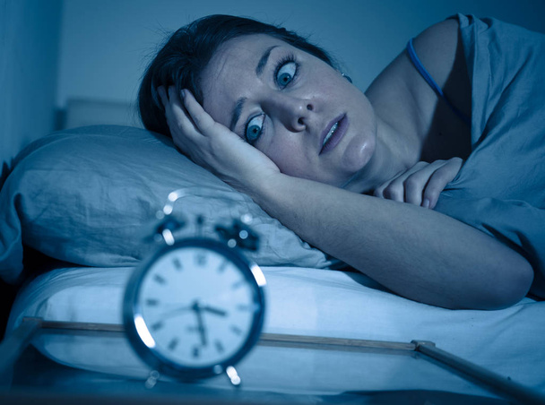 Sleepless and desperate beautiful caucasian woman awake at night not able to sleep, feeling frustrated and worried looking at clock suffering from insomnia in sleep disorder concept. - Foto, Imagem