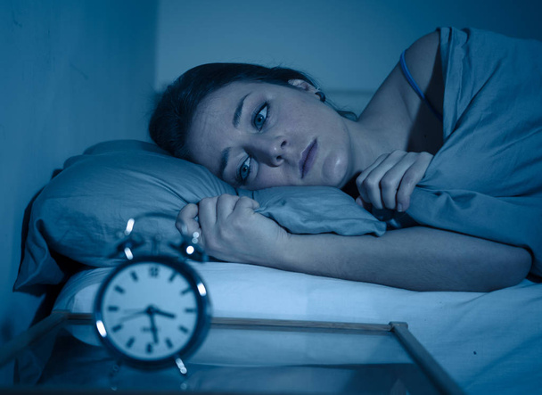 Sleepless and desperate beautiful caucasian woman awake at night not able to sleep, feeling frustrated and worried looking at clock suffering from insomnia in sleep disorder concept. - Φωτογραφία, εικόνα