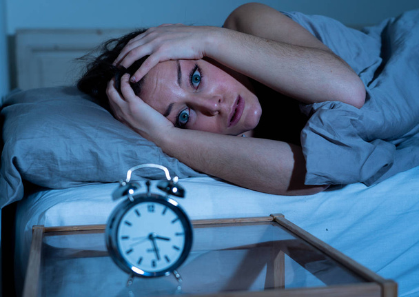 Sleepless and desperate beautiful caucasian woman awake at night not able to sleep, feeling frustrated and worried looking at clock suffering from insomnia in sleep disorder concept. - Fotoğraf, Görsel