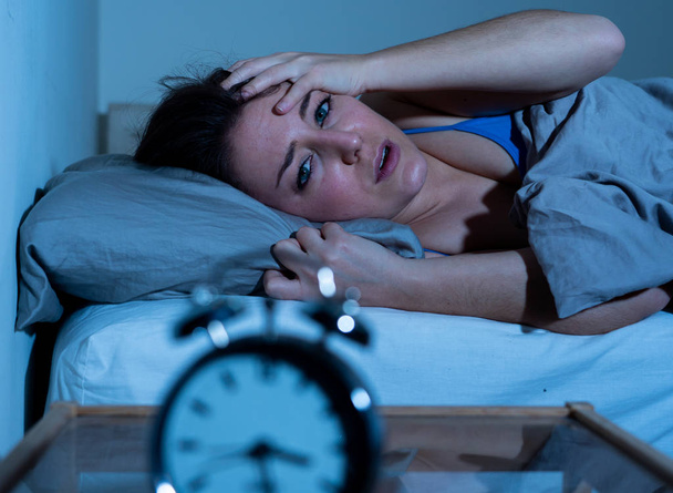 Nieprzespanych i desperate piękna kaukaski kobieta obudzony w nocy nie mógł spać, uczucie frustracji i martwi się, patrząc na zegar, cierpiących na bezsenność w koncepcji zaburzenia snu. - Zdjęcie, obraz