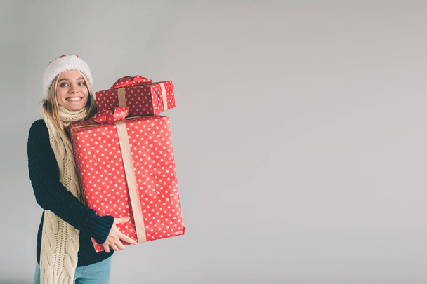 Женщина в рождественской шляпе и в очках с подарками на белом фоне. Девушка в белой рубашке, студия
 - Фото, изображение