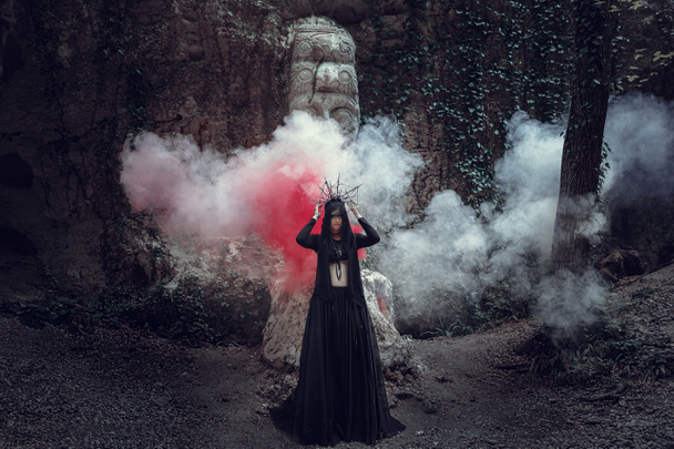 Een mooie vrouw met bleke huid in een zwarte jurk en de zwarte crownk. Gothic look. Outfit voor halloween. - Foto, afbeelding