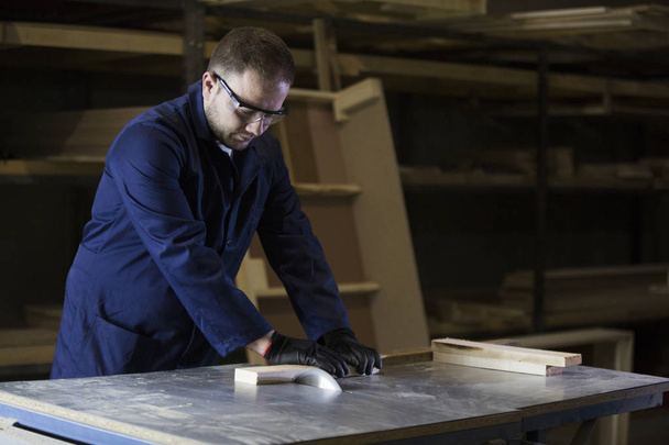 Молодий чоловік на меблевій фабриці вирізає дерев'яні шматочки для дивана
 - Фото, зображення