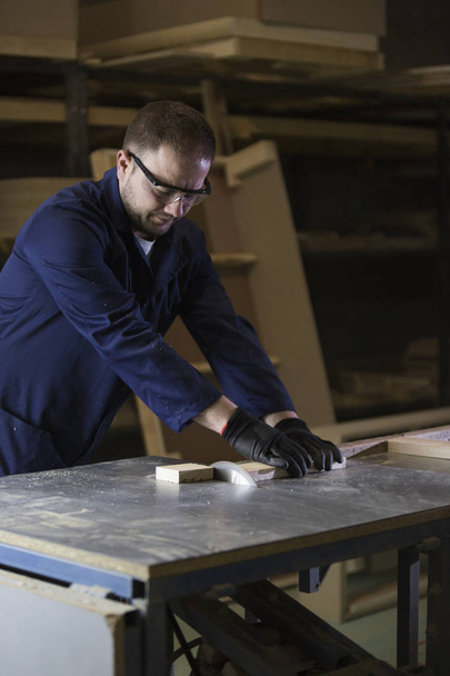 Молодой человек на мебельной фабрике режет деревянные детали для дивана
 - Фото, изображение