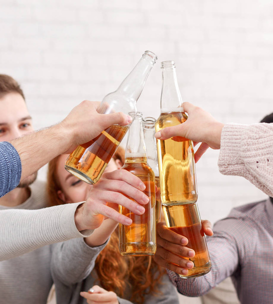 Friends clinking beer bottles, having home party - Фото, изображение