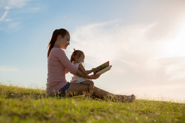 Anya és lánya időt együtt olvasott, miközben ül a parkban. - Fotó, kép