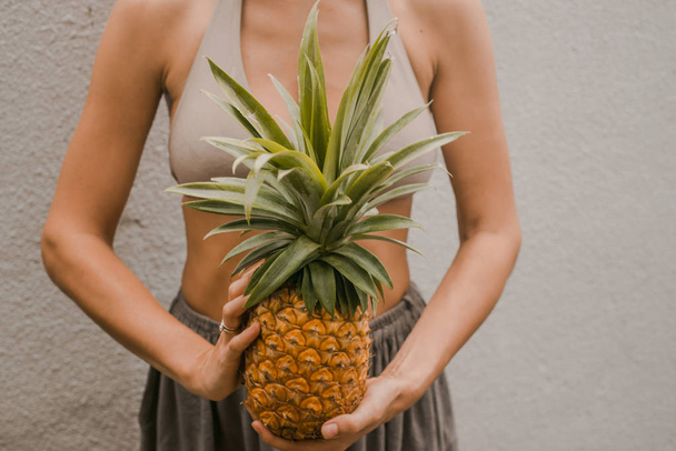 woman in boho clothes keep the tropical fruit pineapple in hands - Фото, зображення