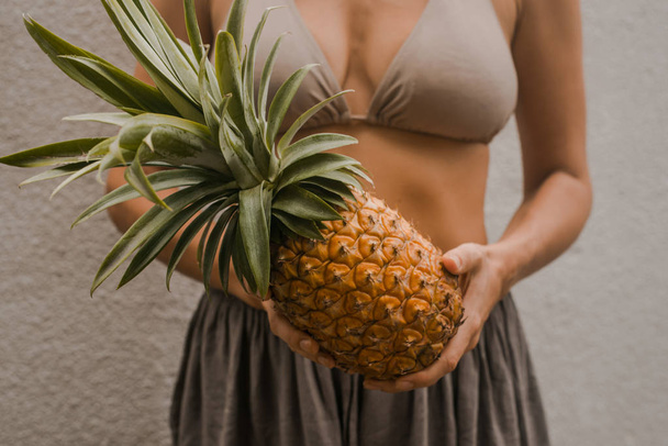 woman in boho clothes keep the tropical fruit pineapple in hands - Foto, Imagen