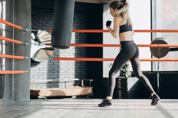Kickboxing woman in airpods training punching bag in fitness studio fierce strength fit body - Fotoğraf, Görsel
