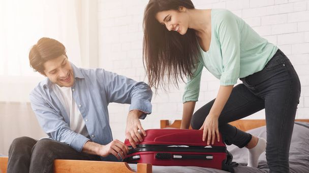 Couple trying to close valise, packing suitcase - Foto, Imagen
